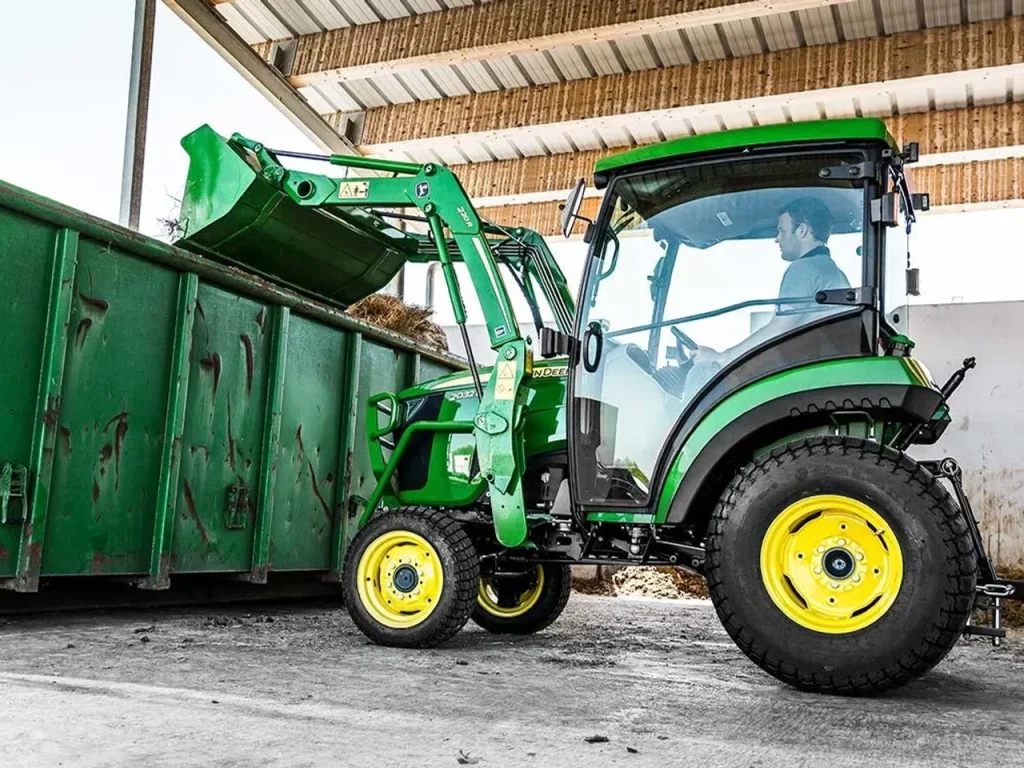 John Deere 2032R compact tractor with 220R front loader tipping a bucket into a trailer